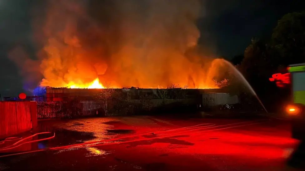 Flames and smoke rising from a building at night as firefighters spray water on it